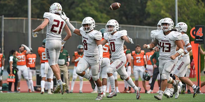 Dominic Corado (#8) celebrates on the field after intercepting a pass as teammates celebrate nearby.
